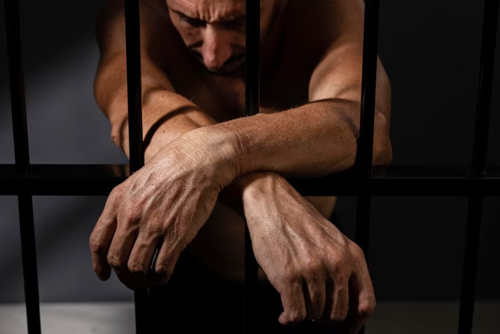 a man in a jail cell with his hands behind his back.