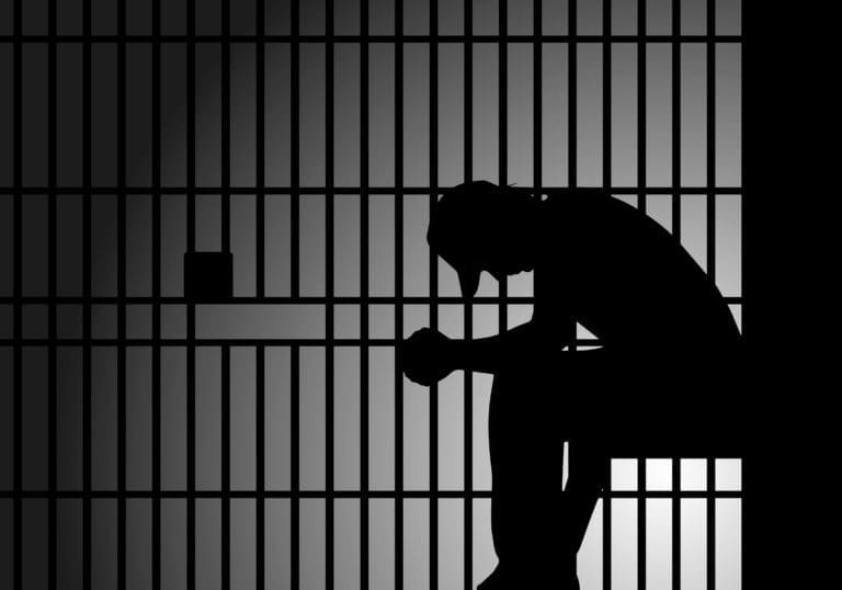 A silhouette of a prisoner sitting in a jail cell.