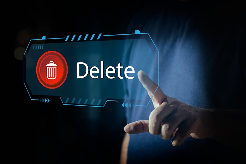 A person’s hand is about to press a digital button with a red trash can icon and the word "Delete" on a futuristic transparent screen interface, symbolizing the action to remove court records seamlessly.
