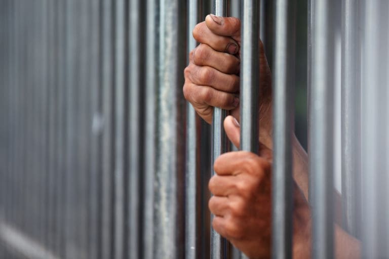A man's hand is reaching out of a metal barricade.