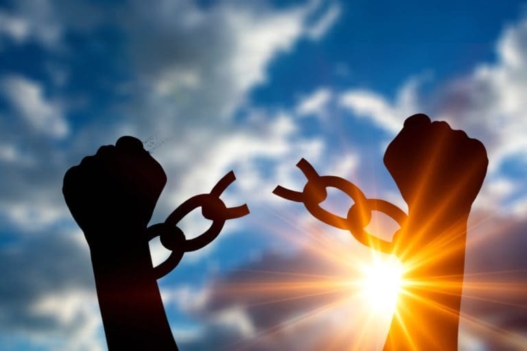 A silhouette of two hands holding a chain against a blue sky.