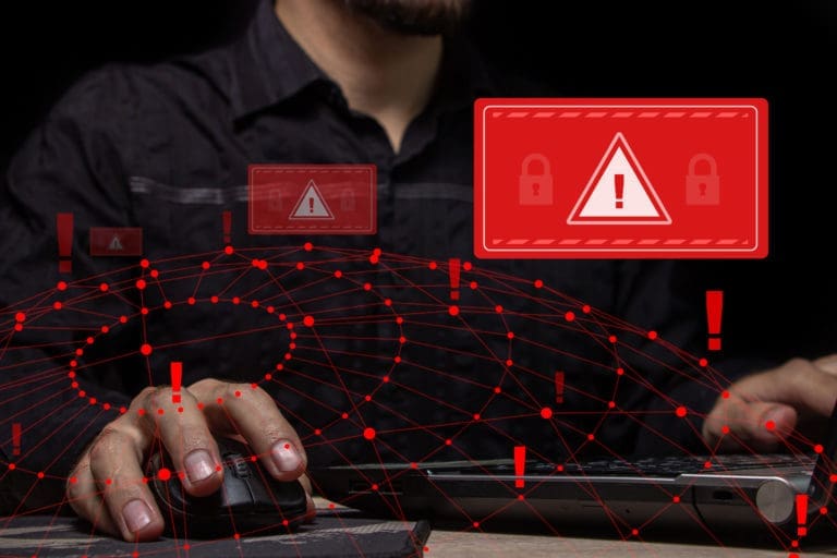 A man typing on a computer with a red warning sign.
