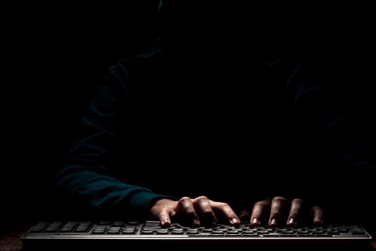 A person in a hoodie typing on a computer keyboard.