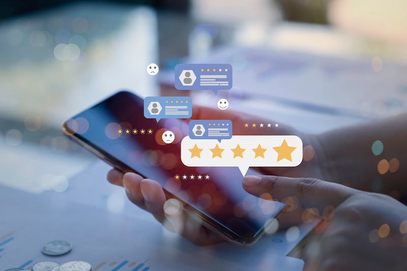 A hand holds a smartphone, with digital icons of chat bubbles, user profiles, emoji faces, and a five-star rating overlayed—highlighting how online reviews can shape or lead to a damaged reputation.