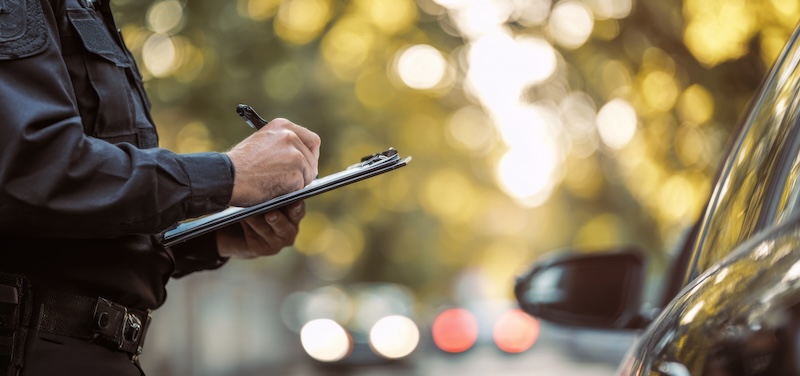 A police officer stands next to a car and writes a ticket.